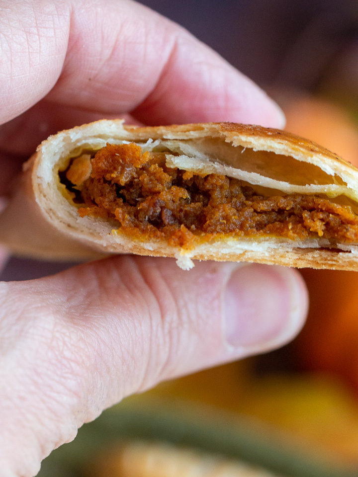 Pumpkin hand pie in a hand cut in half showing the delicious pumpkin filling and flaky crust.