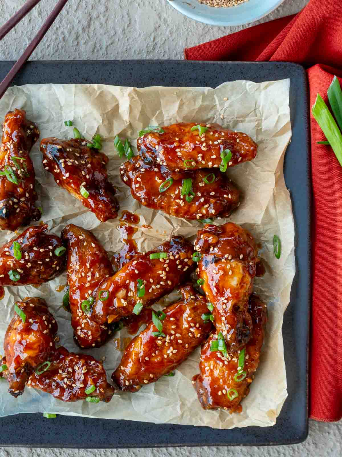 Baked General Tso's Chicken wings laying on a black plate lined with parchment paper. 