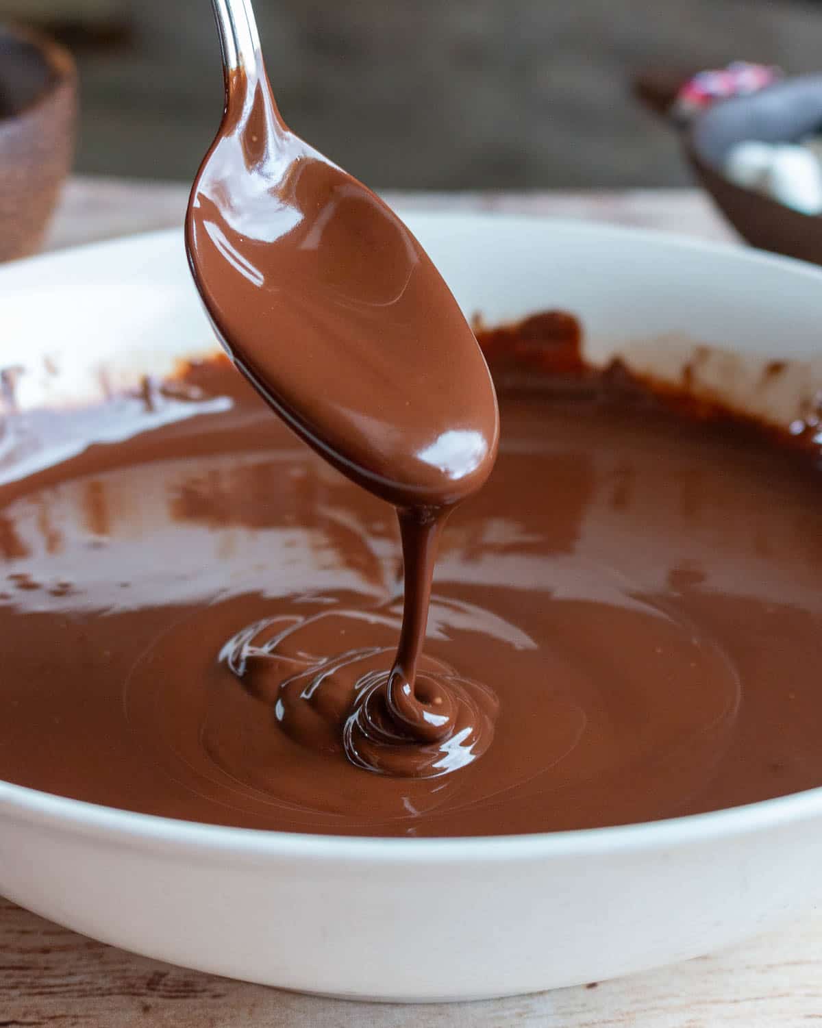 Melted vegan dark chocolate drizzled from a spoon in a white bowl.