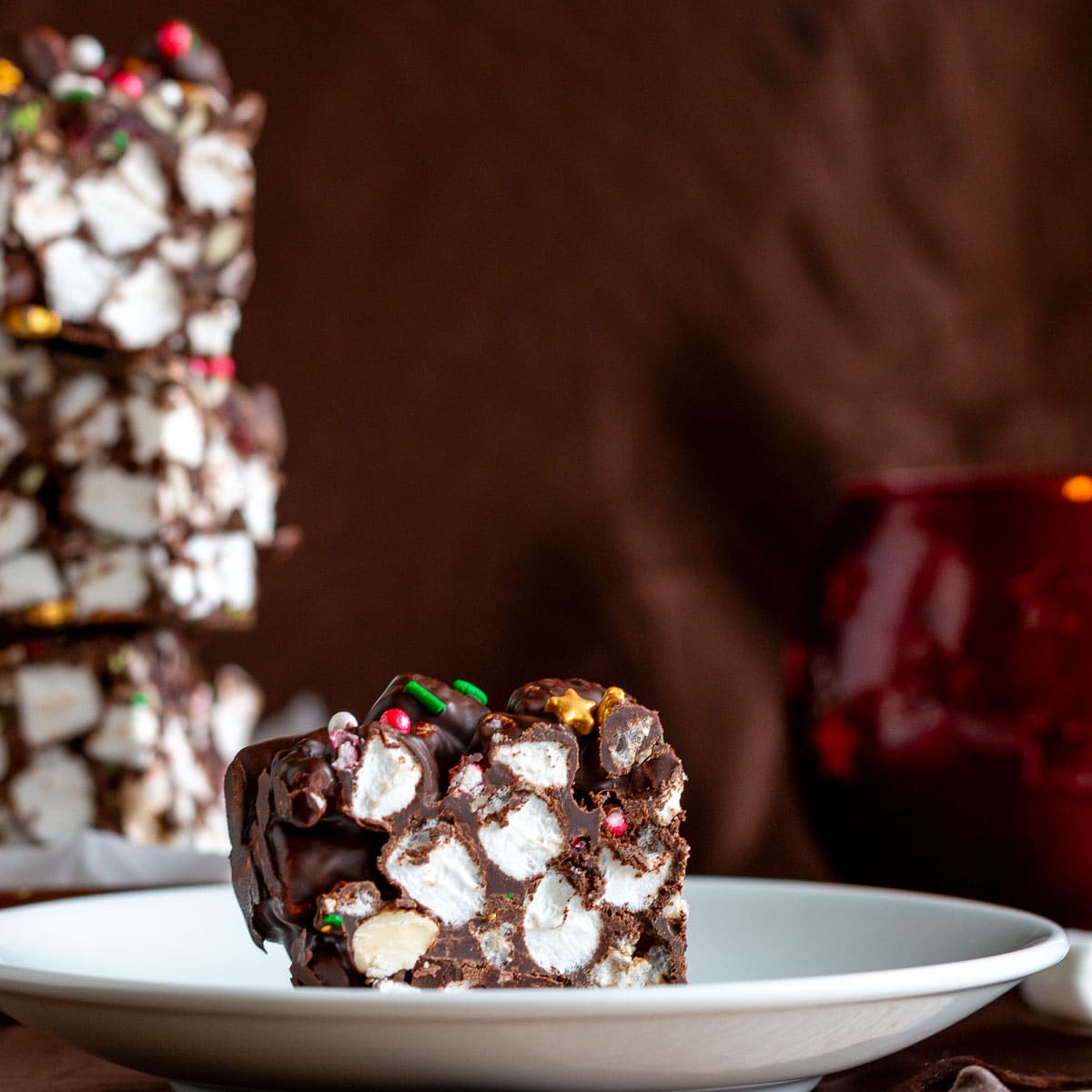 A slice of chocolate rice cake rocky road on a white plate with more candy bars in the background. 