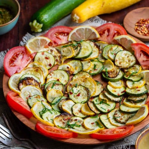 Air fryer zucchini and squash on a wooden plate garnished with tomatoes and lemons.