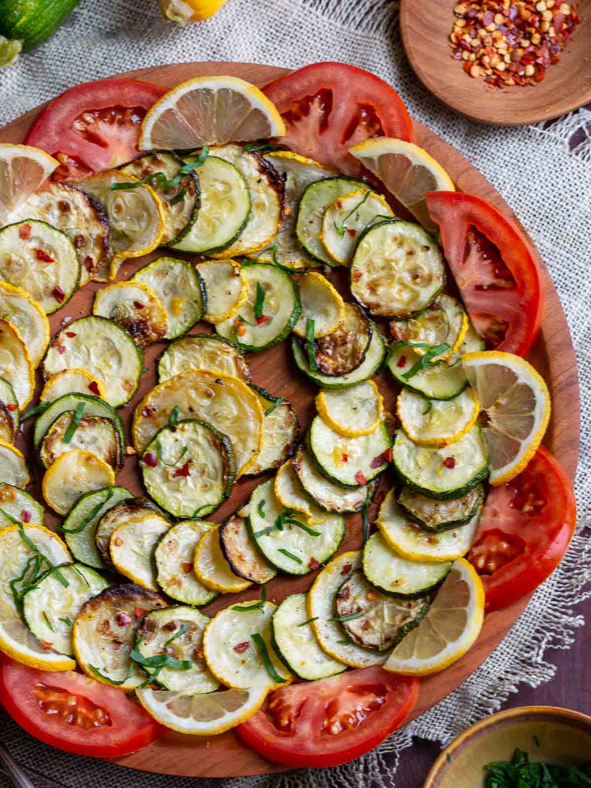 Summer air fried squash layered in a circular design and garnished with tomatoes, lemon zest and a side of red pepper flakes. 