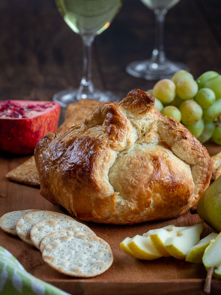 Whole savory baked brie in puff pastry just baked with crackers, wine and fruits to serve on side. 