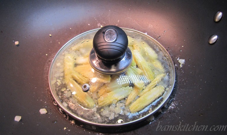 baby corn getting steamed in the wok with a lid.