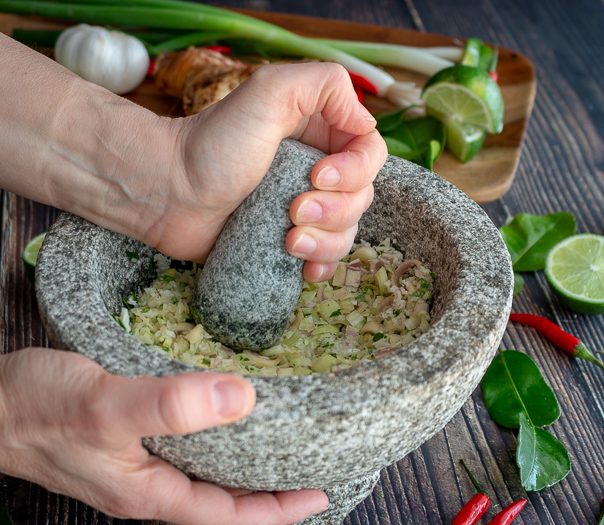 With a huge mortar and pestle crushing up lemongrass and aromatics.