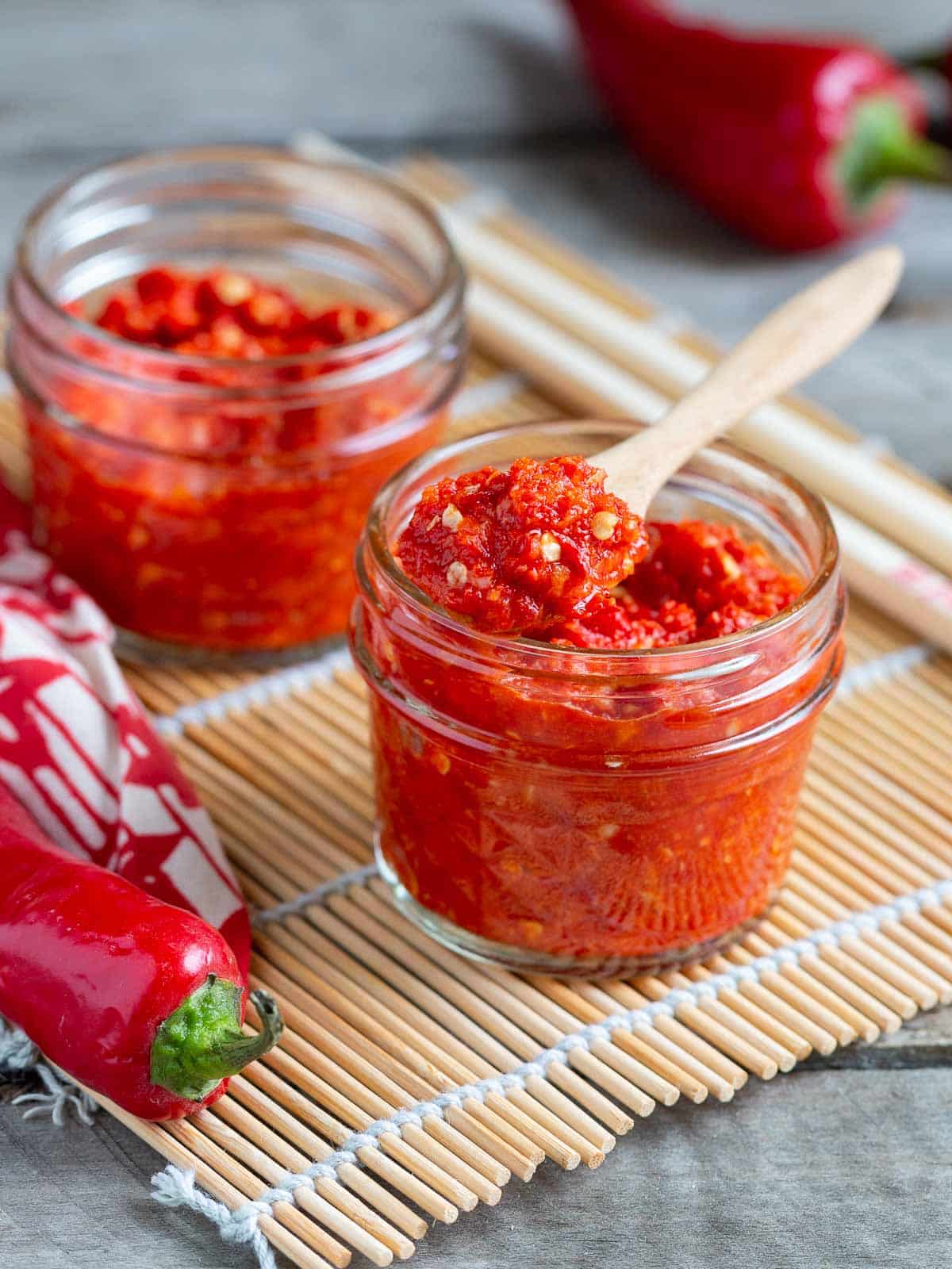 Chile garlic sauce in jars with a wooden spoon scooping out a teaspoon. 