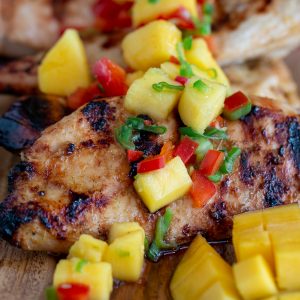 Grilled Mango chicken breasts topped with fresh mango salsa on a wooden board.