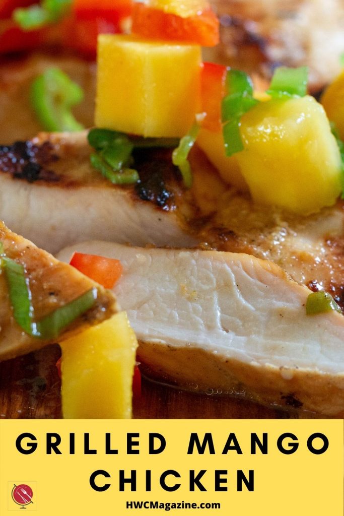 Grilled Mango chicken breasts topped with fresh mango salsa on a wooden board. Sliced juicy chicken.