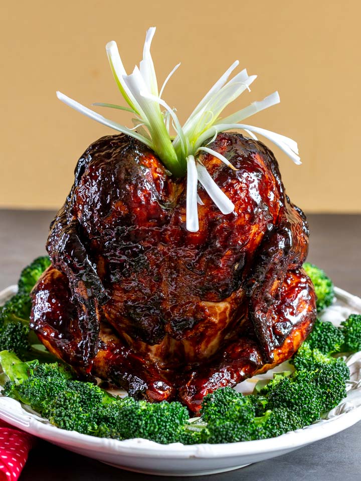 Chciken with Peking sauce on a white plate surrounded by stir fried broccoli.