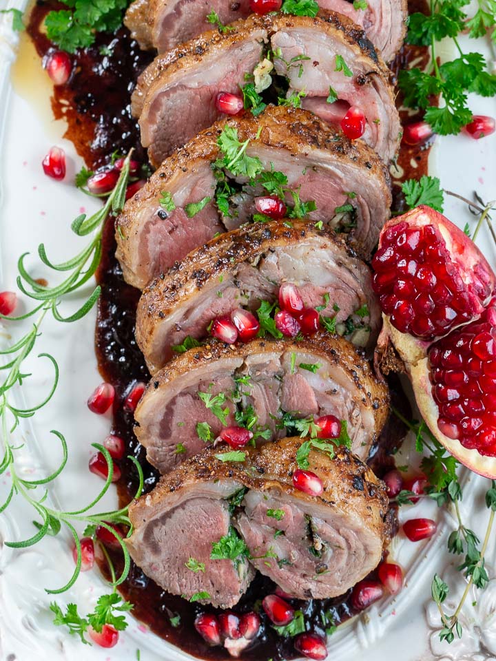 Top down shot of roasted lamb loin topped with pomegranate seeds and herbs.