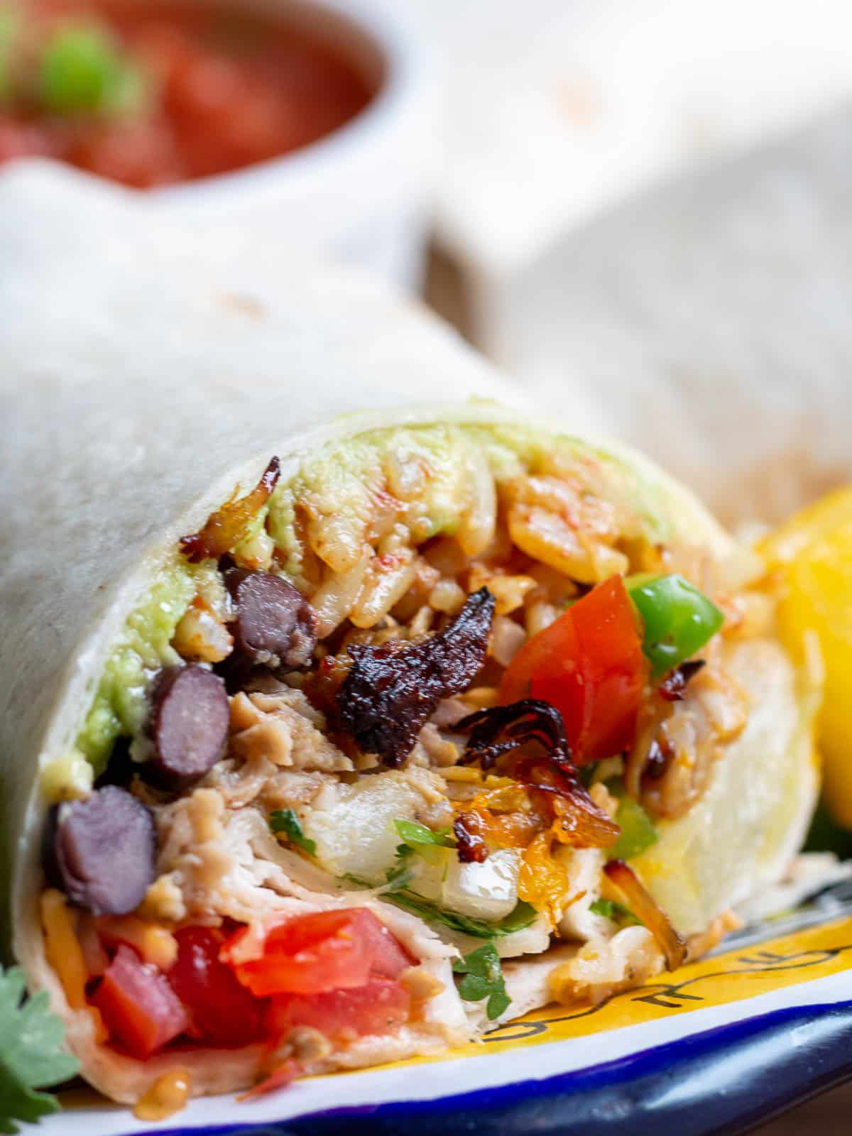 Close up of a wrapped carnitas burrito with all the toppings cut in half to show all the fillings like black beans, guacamole and pineapple slaw.