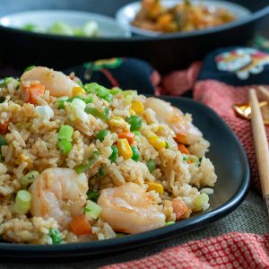 Resturant style Hong kong Fried rice with shrimp on a black plate with chopsticks.
