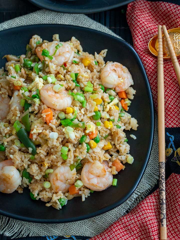 Top down shot showing the Hong Kong Fried rice with the shrimp all the vegetables delicious displayed in a black plate with chopsticks.