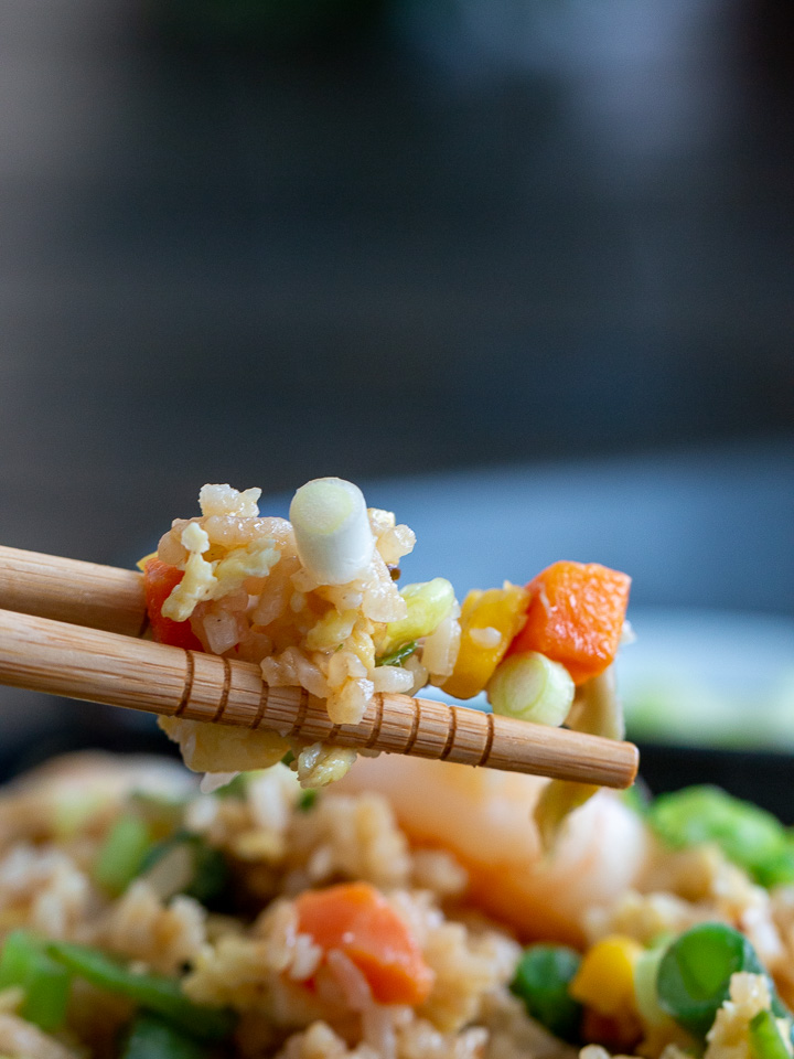 A bite shot showing the individual grains of rice, small vegetables and snow flakes of egg in the fried rice.