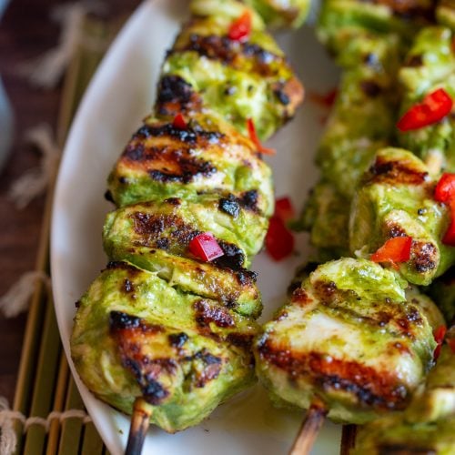 Grilled green chicken kabab in a white plate sprinkled with red chilis.