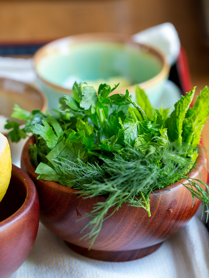 Fresh green herbs in a wooden bowl.