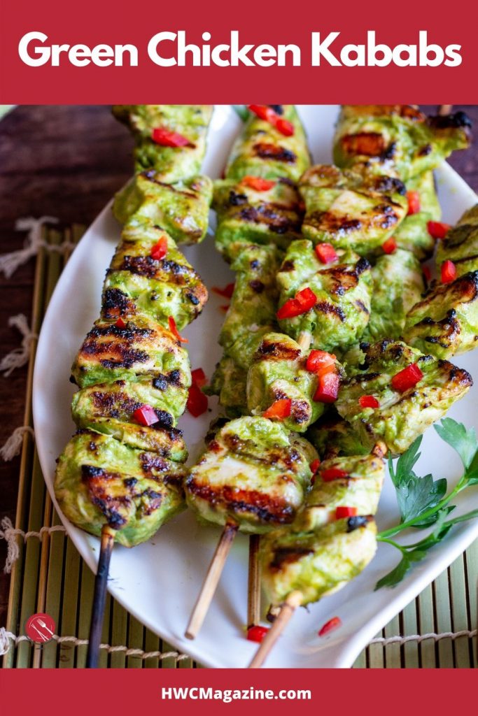 On a green mat with a white plate filled with many chicken skewers and garnished with chili and parsley.
