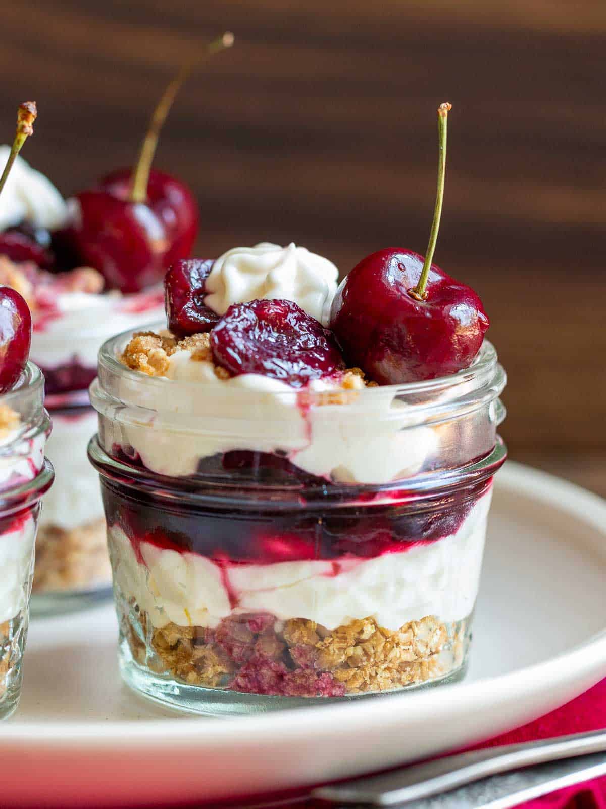 3 gluten free no bake cheesecakes with saucy bourbon cherries in a jar on a white plate.