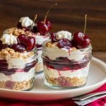 3 no bake boozy cherry cheesecake jars topped with bourbon cherry compote on a white plate.