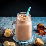 Creamy rich chocolate peanut butter smoothie topped with bananas and unsweetened chocolate cocoa powder. Surrounded by chopped bananas , peanut butter.