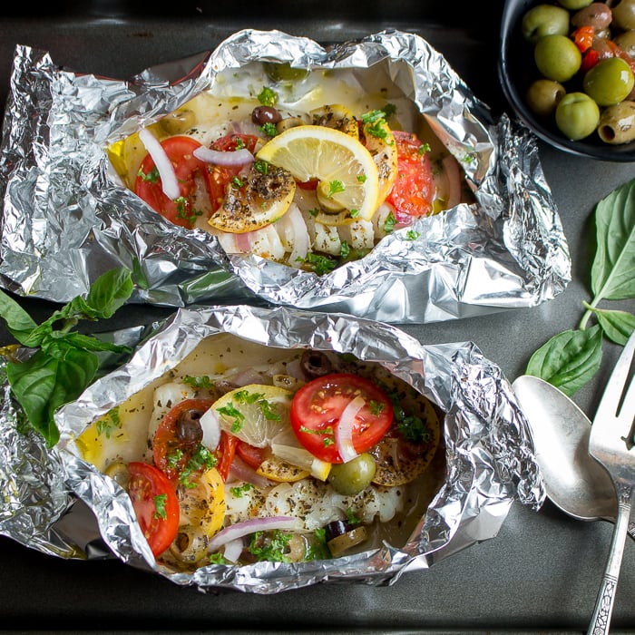 2 Mediterranean Red Snapper Packets opened to show the fish and all the toppings. A bowl of olives nearby.