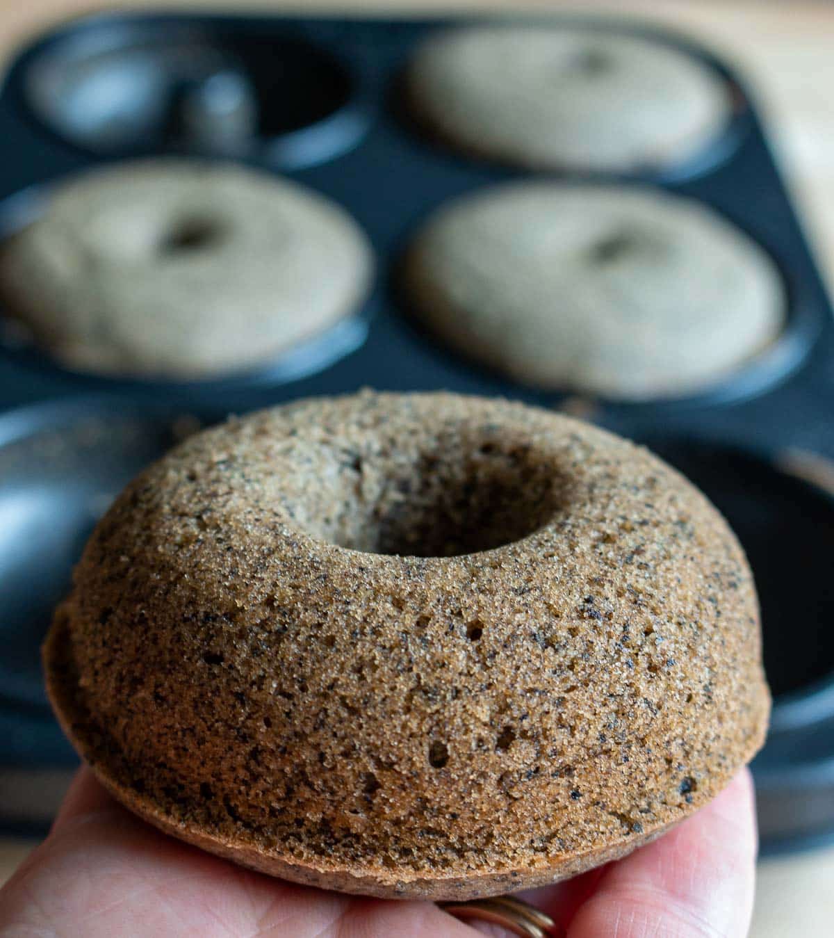 Black sesame mochi donut fresh out of the oven held in a hand. 