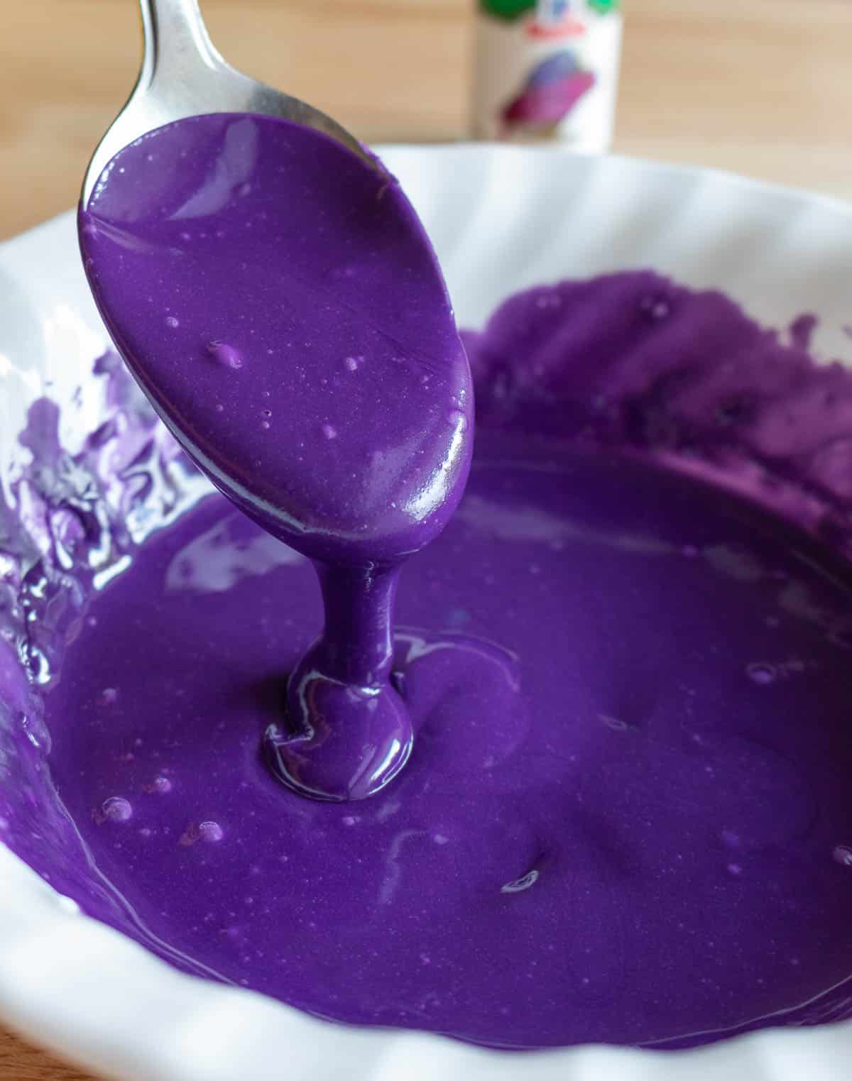 Ube glaze drizzling from a spoon into a white bowl.