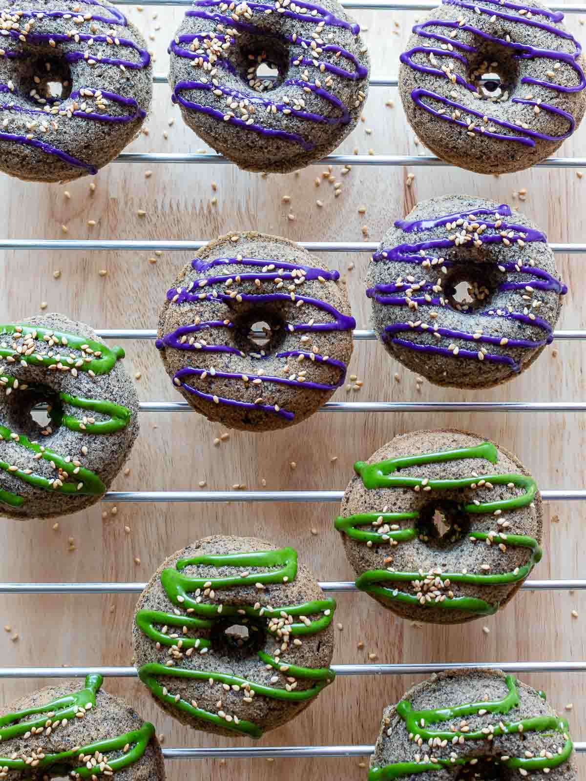Matcha and Ube glazed baked black sesame mochi donuts drying on a wire rack.
