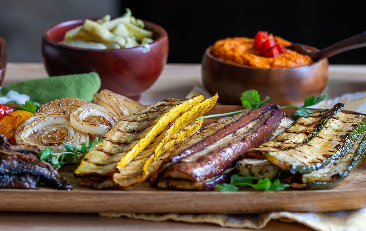 Grilled vegetables, hummus and artichokes and many other ingredients in bowls.