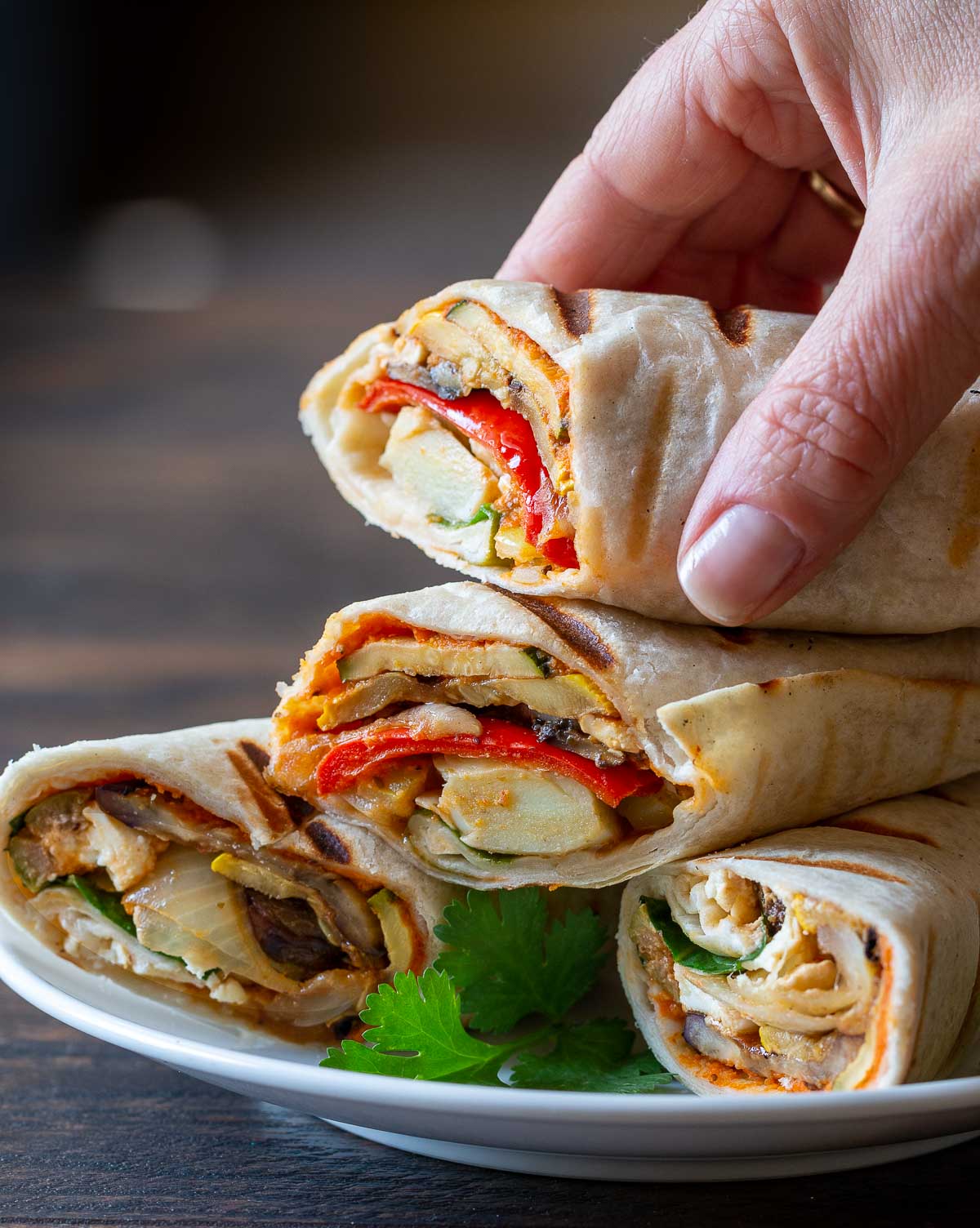Grilled vegetable wraps with hummus on a white plate cut in half and being served to guests.