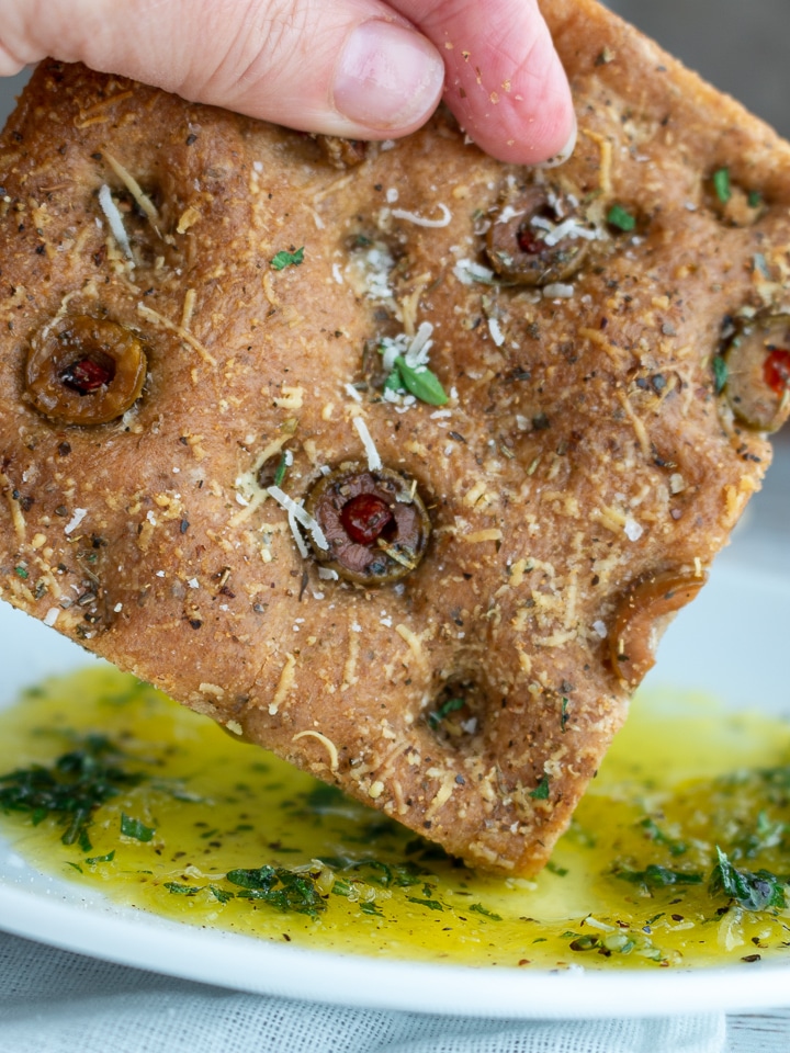 Whole wheat herb focaccia bread getting dipped into herb oil.