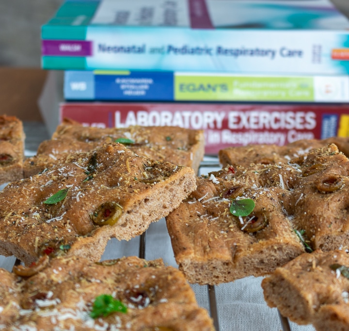 Focaccia bread cooling on a rack with respiratory care books piled high in the background.