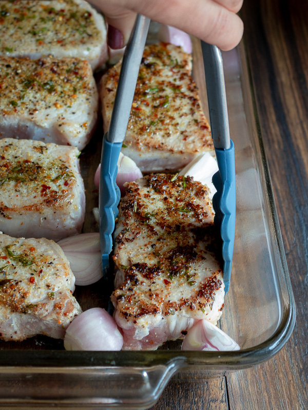 Placing a tray of seared pork chops into a pan to go into the oven.