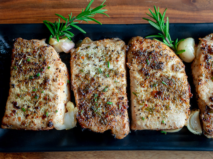 Top down shot of three pork chops on a serving plate garnished with fresh rosemary. 