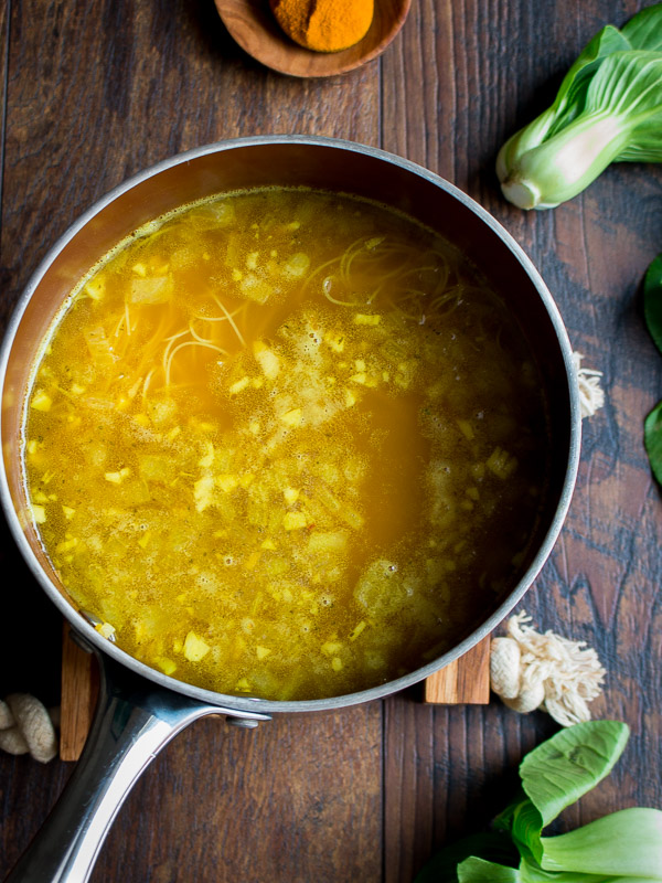 Golden chicken bone broth with aromatics in a pot simmering.