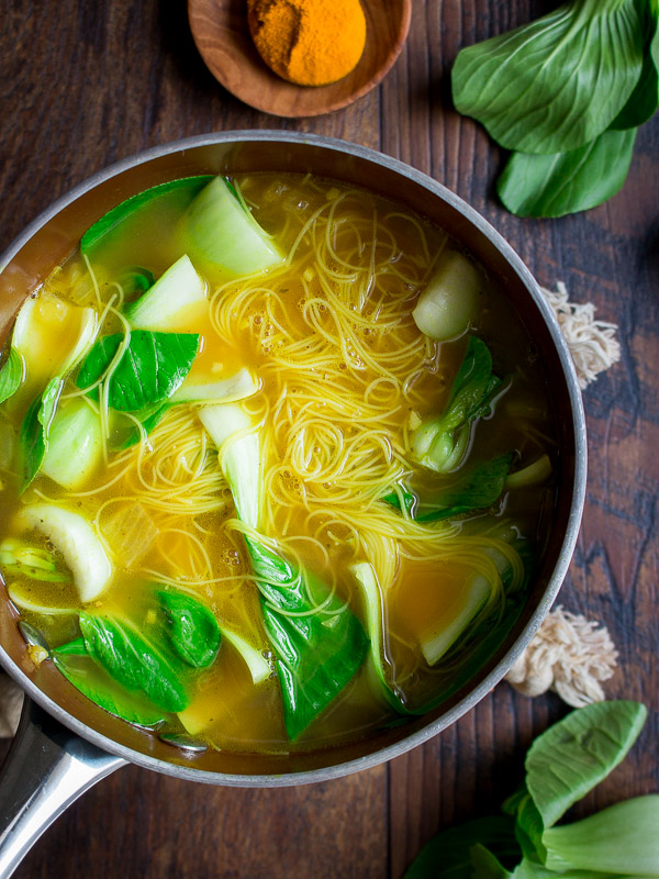 Bok choy and chicken bone broth with simmering noodles in a soup pot. 