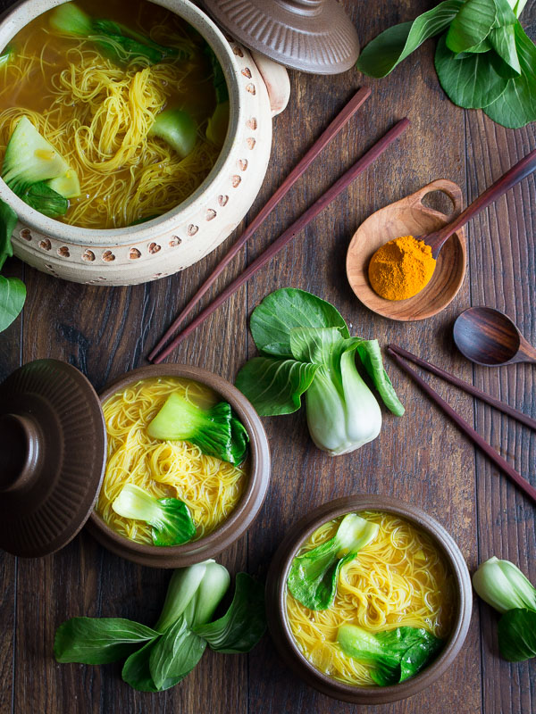 2 bowls of turmeric chicken noodle soup in brown bowls with a big soup pot in the background. 