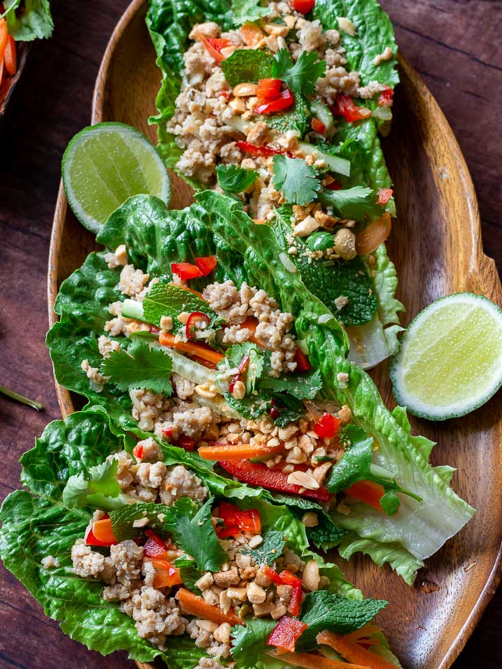 Healthy Chicken Lettuce wraps all prepared with toppings and ready to be served on a wooden Thai platter.