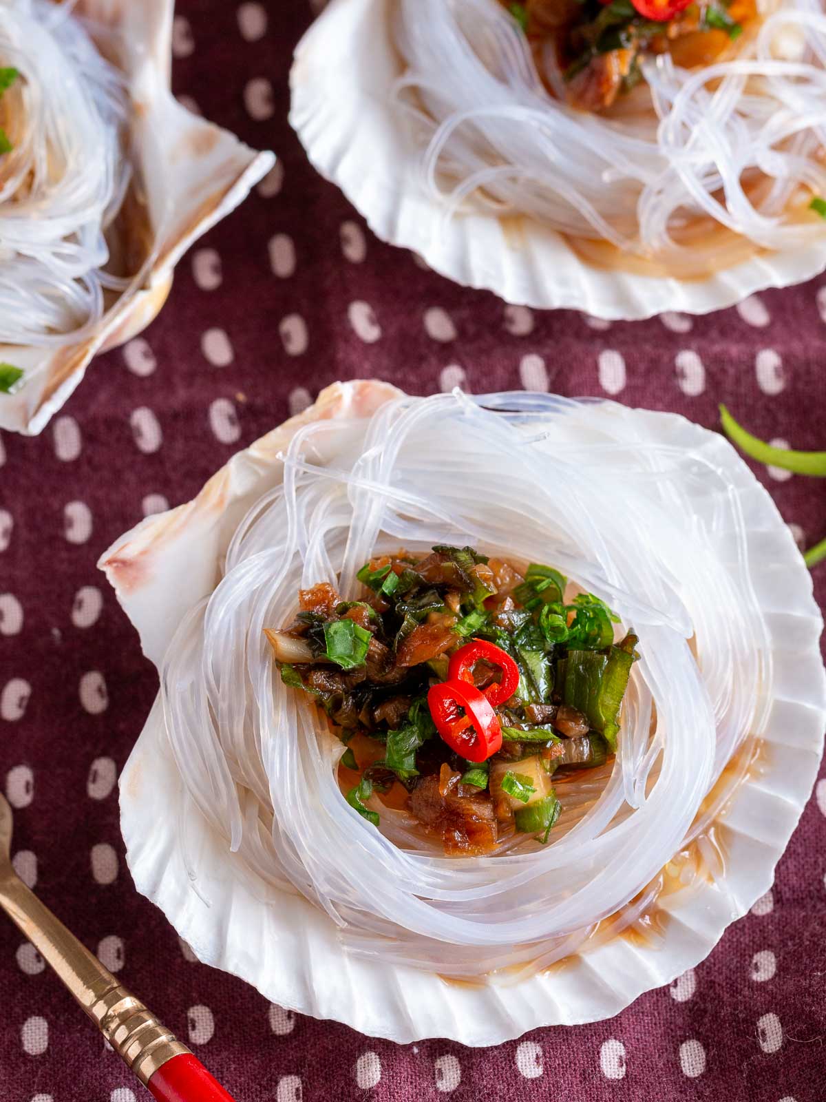 Steamed scallops in shell on a dark brown and white tea towel.