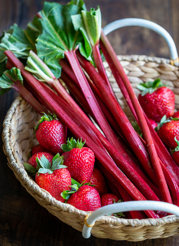 In a woven basket fresh rhubarb stalks and fresh whole strawberries.