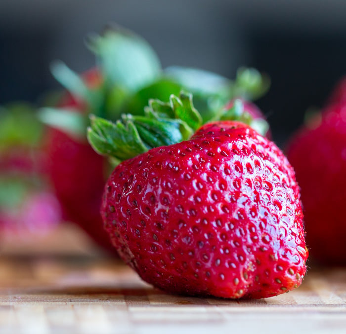 Whole fresh strawberry just washed with drips of water glistening on a bamboo cutting board. 