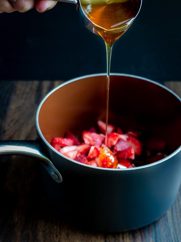 Honey being drizzled over strawberries and rhubarb in a sauce pan.