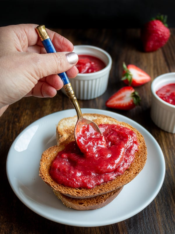 Strawberry rhubarb refrigerator jam getting spooned over 2 slices of toast.