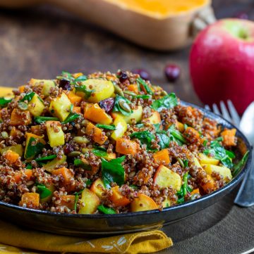 Quinoa Harvest Salad in a black bowl with apples and butternut squash in the background.
