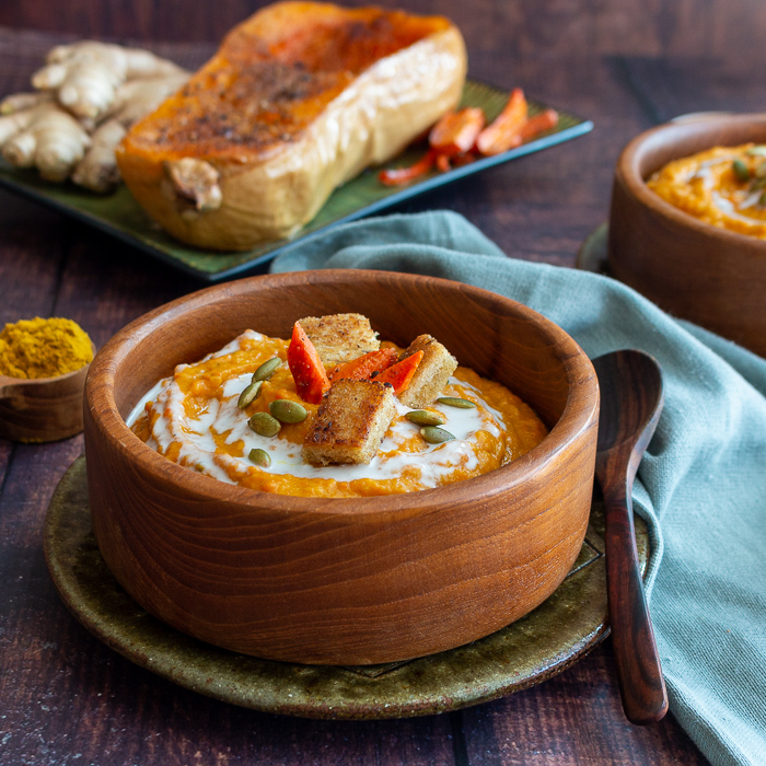 Bowl of soup with a spoonful of curry powder and a roasted butternut squash next to it.