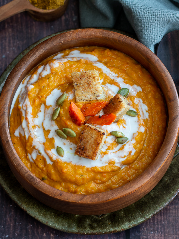 Top down close up shot of Finished Butternut Squash and Carrot ginger soup garnished with pumpkin seeds, homemade gluten-free croutons and coconut milk.