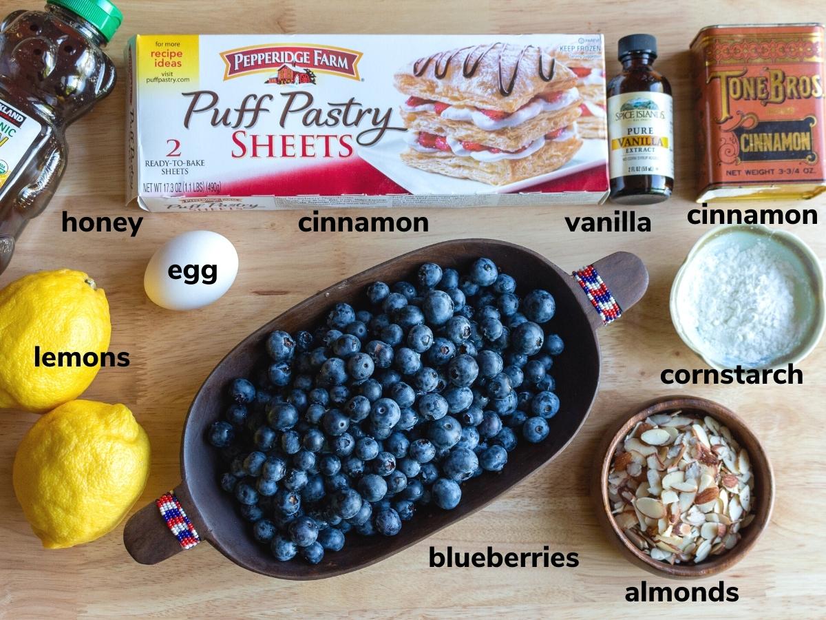 Ingredients to make rustic mini blueberry galettes on a light wooden table.
