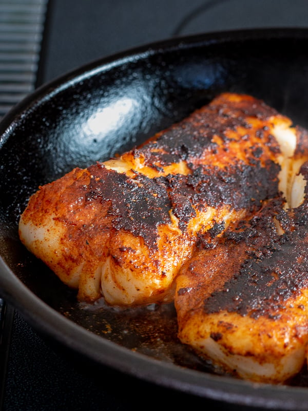 3 cod fillets getting blackened into the iron skillet.