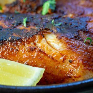 Close up shot of flaky cajun cod with a wedge of lemon.