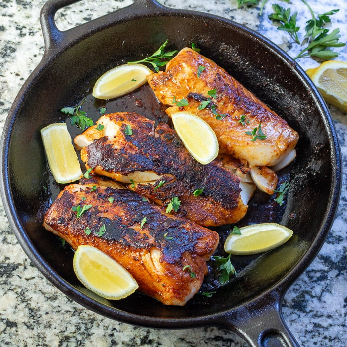 3 fish fillets in an iron skillet garnished with lemons and herbs. 